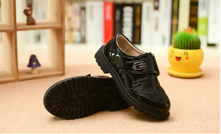 Boys black patent leather shoes with brogue detail featuring a velcro strap ideal for british casual single wear.