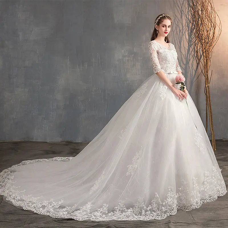 A white lace wedding dress trailing with a high waist, three-quarter length sleeves, and intricate floral embroidery along the hemline.