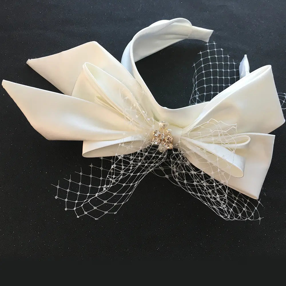 An elegant ivory satin bow headpiece with delicate white lace and a sparkling gold embellishment designed as a fashion bridal wedding satin headband.