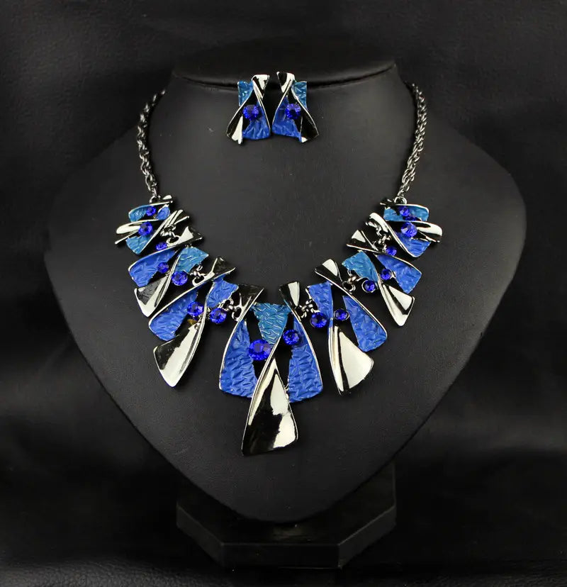 blue and silver metal geometric shape necklace set featuring a layered geometric shape rhinestone pendant accented with small blue gemstones paired with matching shape rhinestone earrings.