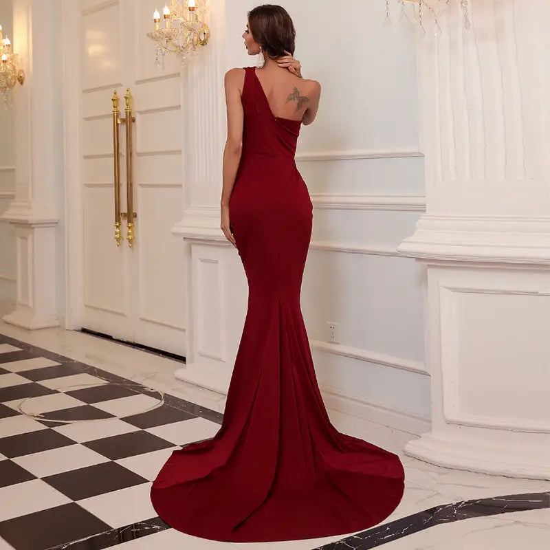 A deep red wine red solid color mermaid style annual meeting dress with a form-fitting silhouette, single shoulder design, and flowing train.