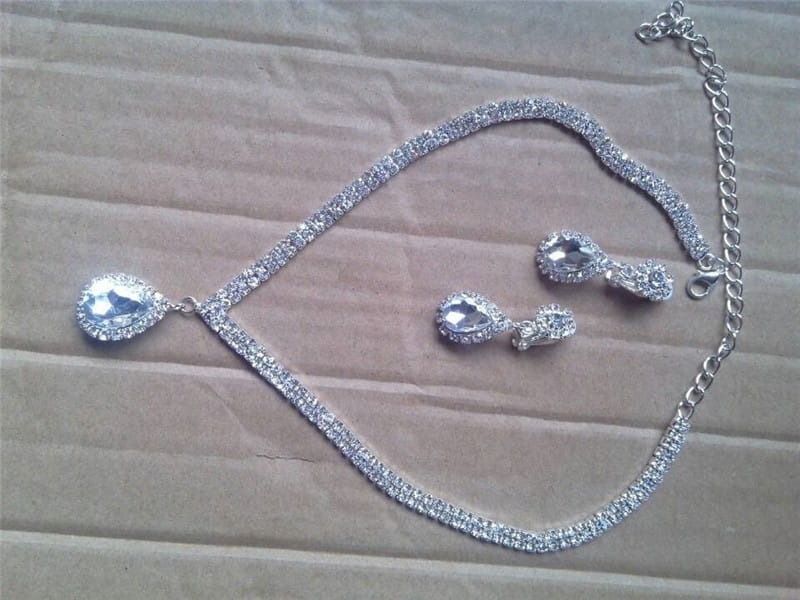 Silver v-shaped crystal bridal jewelry set featuring a silver rhinestone necklace with a teardrop pendant and matching earrings with sparkling crystals along the chain.