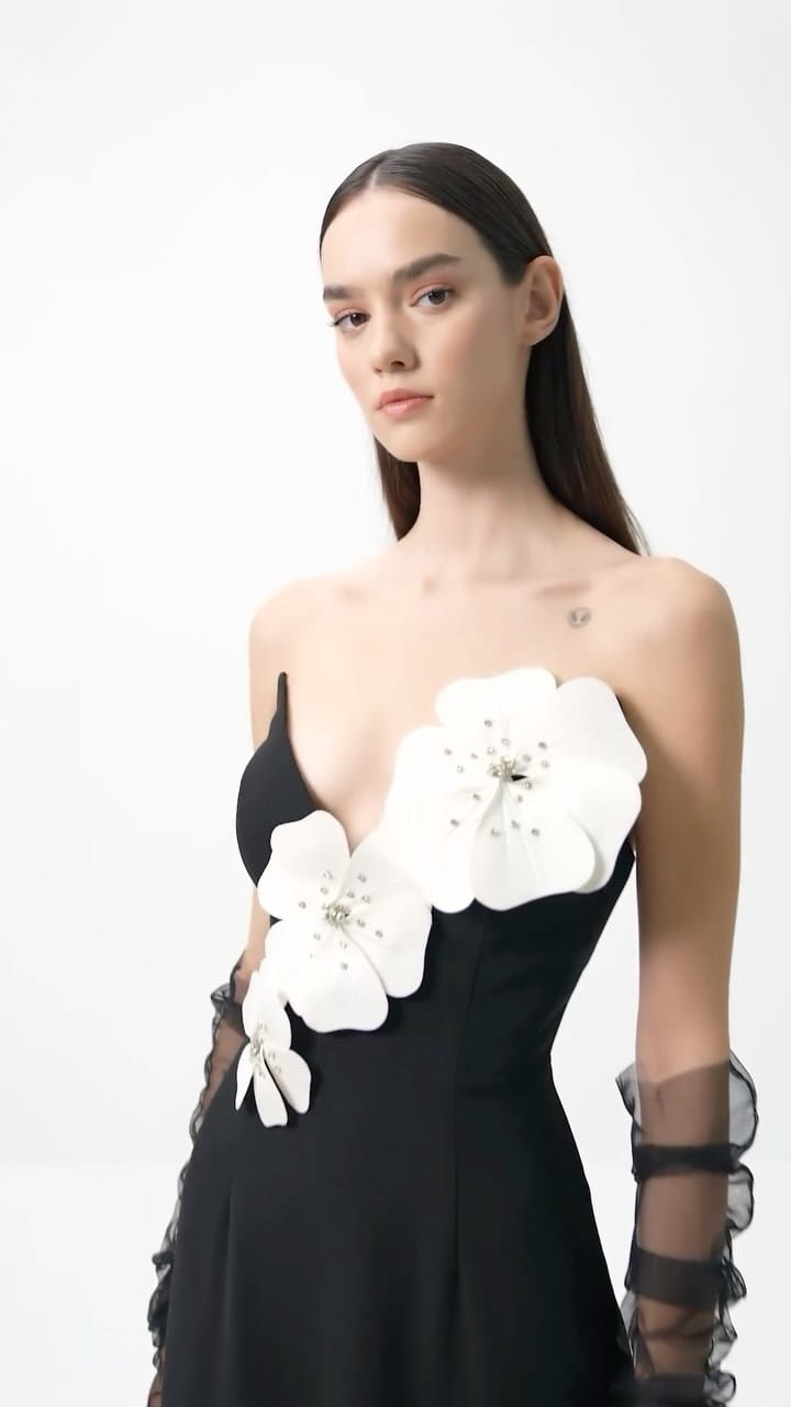 black backless bandage gown featuring large white floral appliqués with sparkling centers and sheer lace detailing on the sleeves showcasing an elegant bandage chest white design