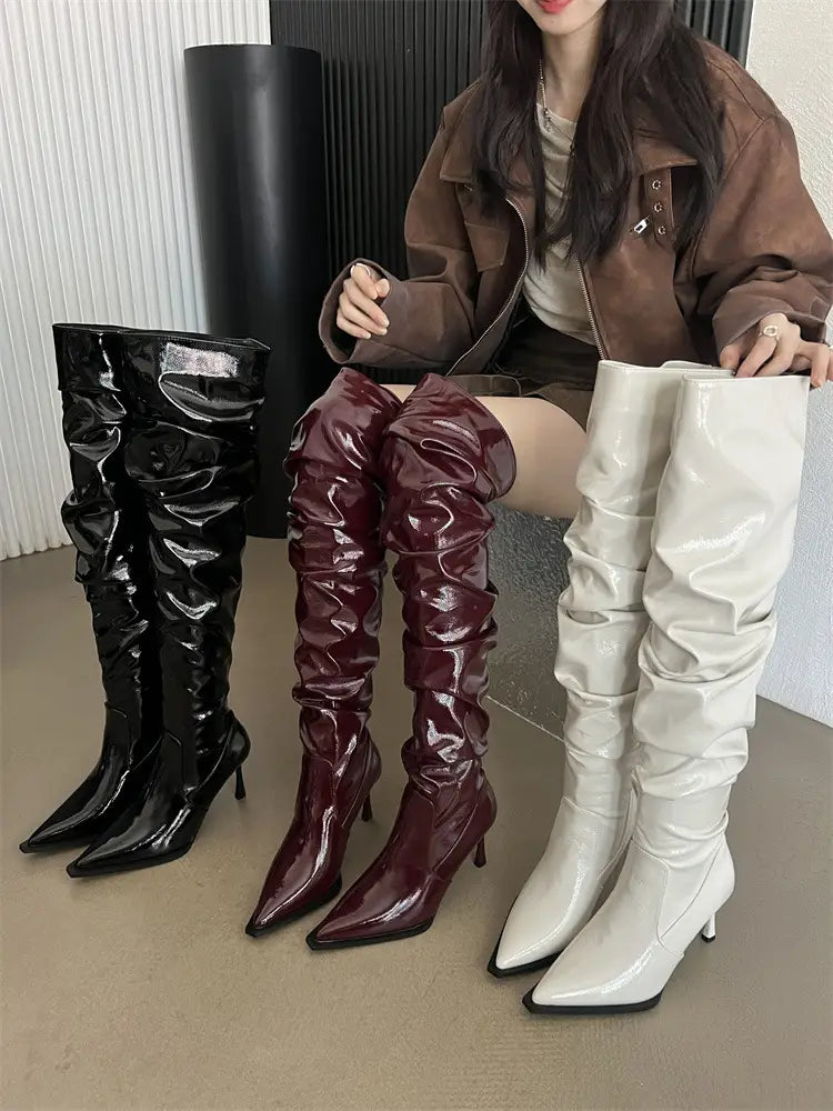 Three pairs of glossy patent stiletto heel pile style thigh high boots in black burgundy and white with ruched over-the-knee design perfect for autumn stiletto heel fashion.