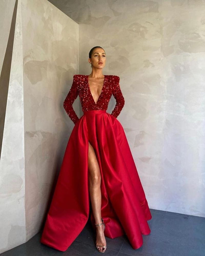 a striking red evening dress made of polyester fiber featuring a sequined bodice, long sleeves, a satin skirt with a high slit, and large posing temperament for formal occasions