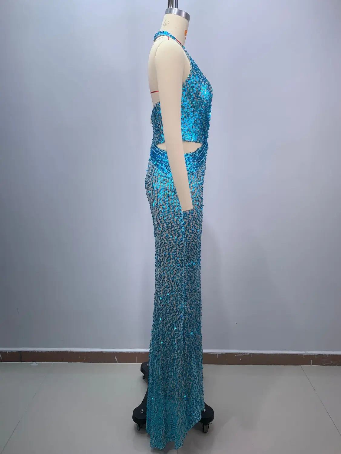 a shimmering turquoise sequined halter-neck slim slimming party stage host mermaid gown with a fitted silhouette and side cutouts displayed on a mannequin