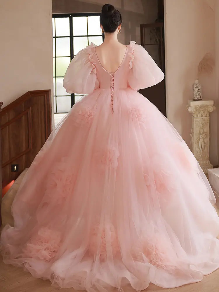 A soft pink high end banquet style host floral tulle gown featuring a voluminous ball gown silhouette with puffy sleeves and floral appliqués.
