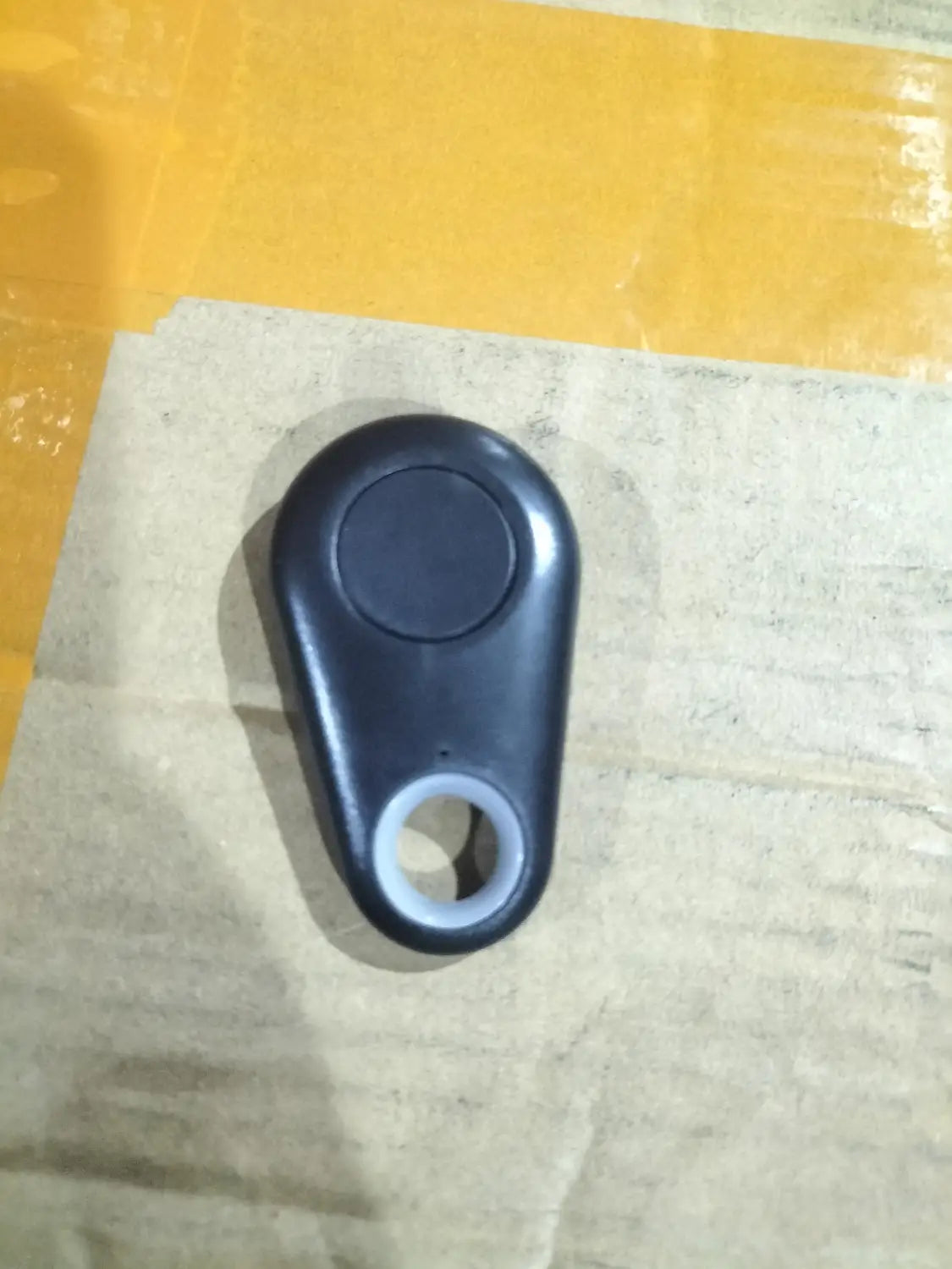 black plastic bluetooth anti lost object finder with a circular button and a ring at the bottom in a water drop shape