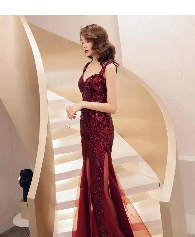 A deep red fishtail long summer evening dress featuring intricate lace detailing and a sheer overlay with long summer sequins sling design.