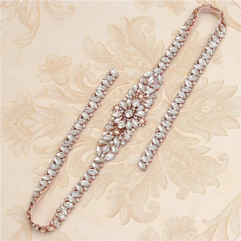 A rose gold-toned rhinestone applique wedding sash featuring a central floral cluster of clear marquise-cut crystals and pearls, designed as wedding dress waist jewelry.