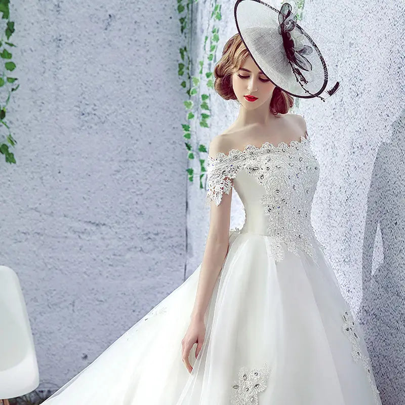 white off-the-shoulder wedding dress bride featuring intricate lace and beaded embellishments paired with a trailing french veil