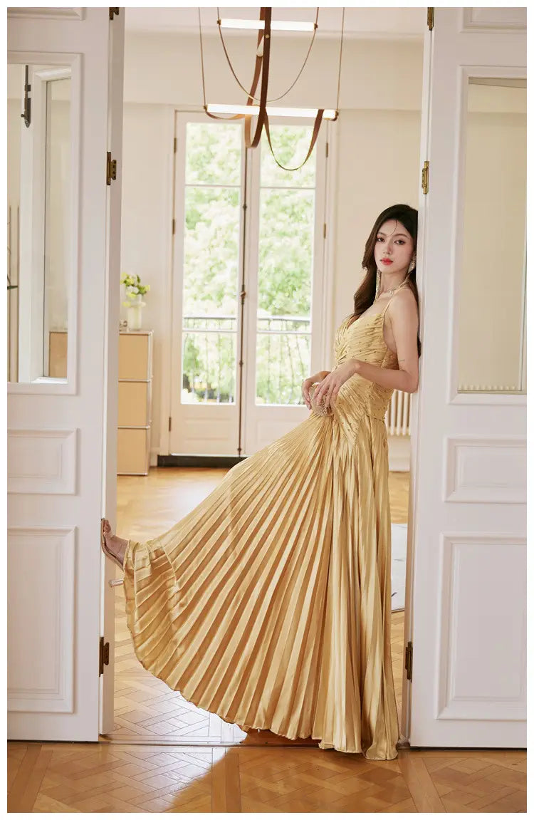 A shimmering gold satin pleated maxi dress with a fitted bodice and flowing skirt designed for heavy industry birthday celebrations.