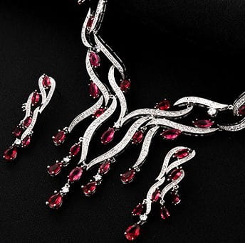 Silver-toned jewelry set featuring a necklace and matching earrings with intricate flowing designs adorned with vibrant red teardrop-shaped gemstones, part of the emerald green crystal jewelry zircon collection.
