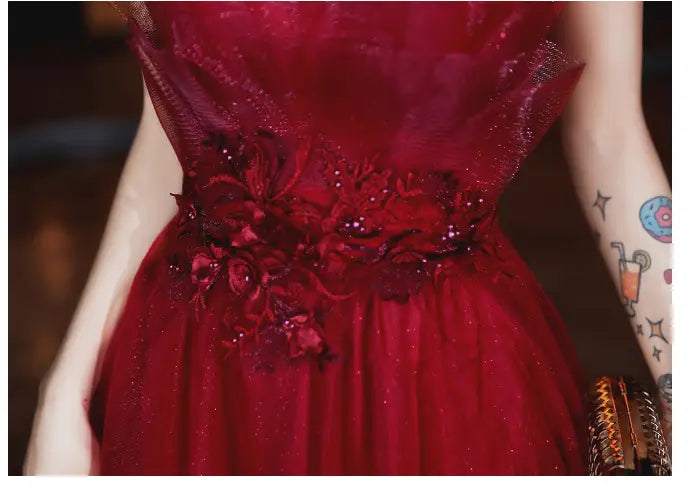 A deep red satin evening dress with glittering tulle adorned with intricate floral appliqués and sparkling beading at the waist designed to wear engagement suspender style.