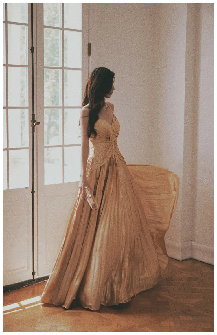 A flowing champagne-colored satin heavy industry birthday dress featuring a fitted bodice and pleated skirt.