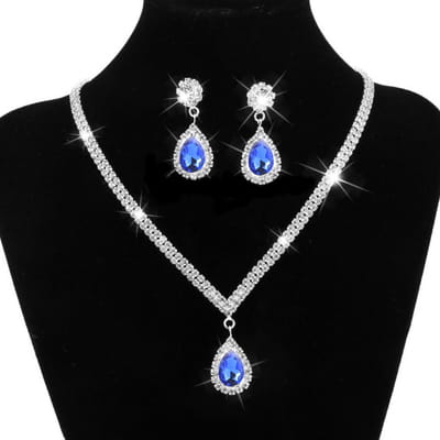 Silver V-shaped crystal bridal jewelry set featuring a sparkling blue teardrop pendant necklace with silver chain and matching earrings adorned with clear crystal accents.