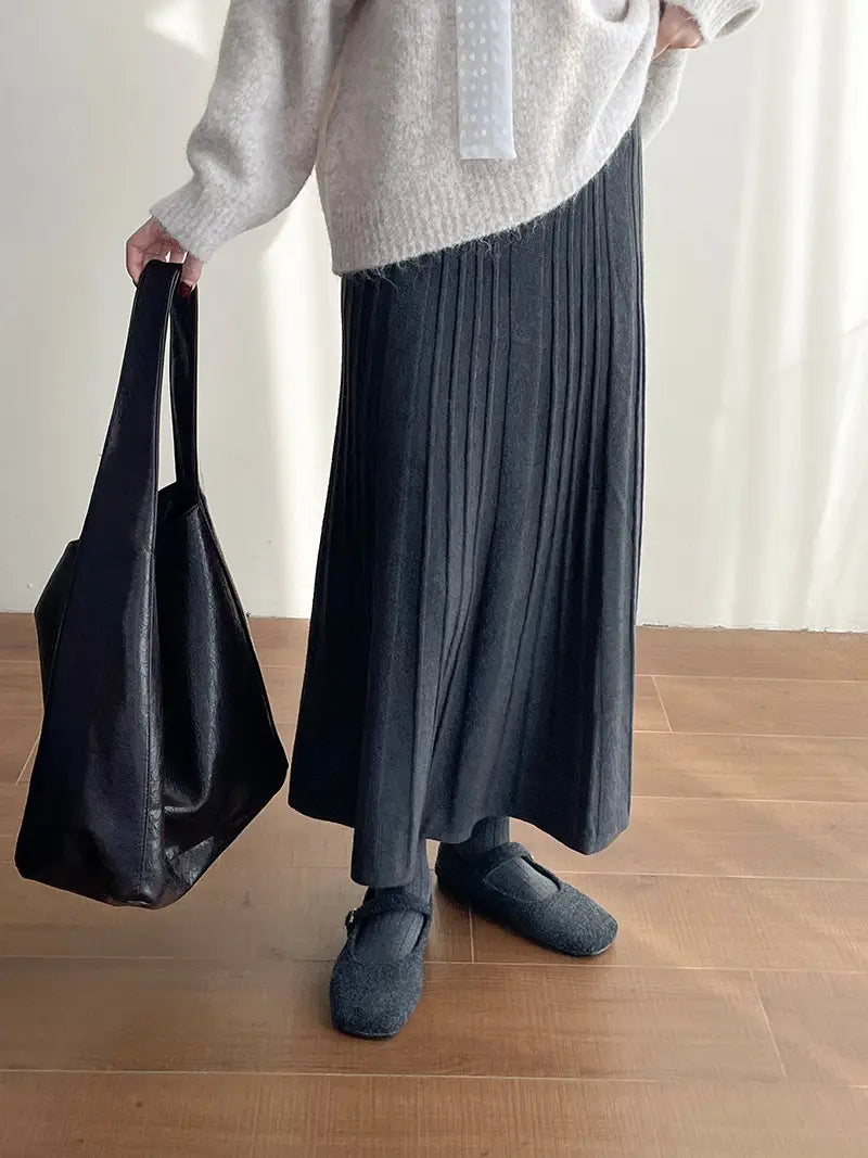black leather tote bag with structured handles and a glossy finish paired with a korean elastic waist knitted pleated midi skirt.