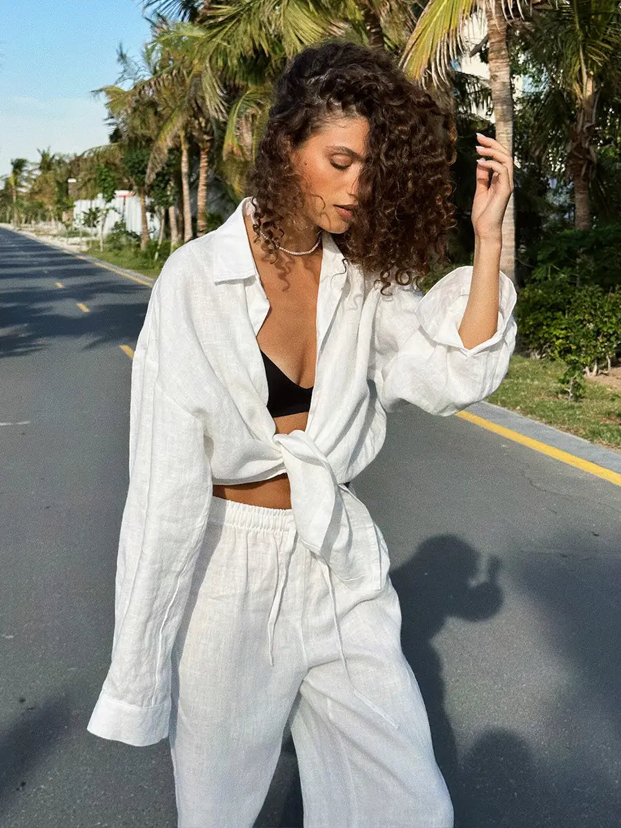 White linen long sleeve shirt with relaxed oversized fit and front knot detail paired with cotton shirt trousers suit.