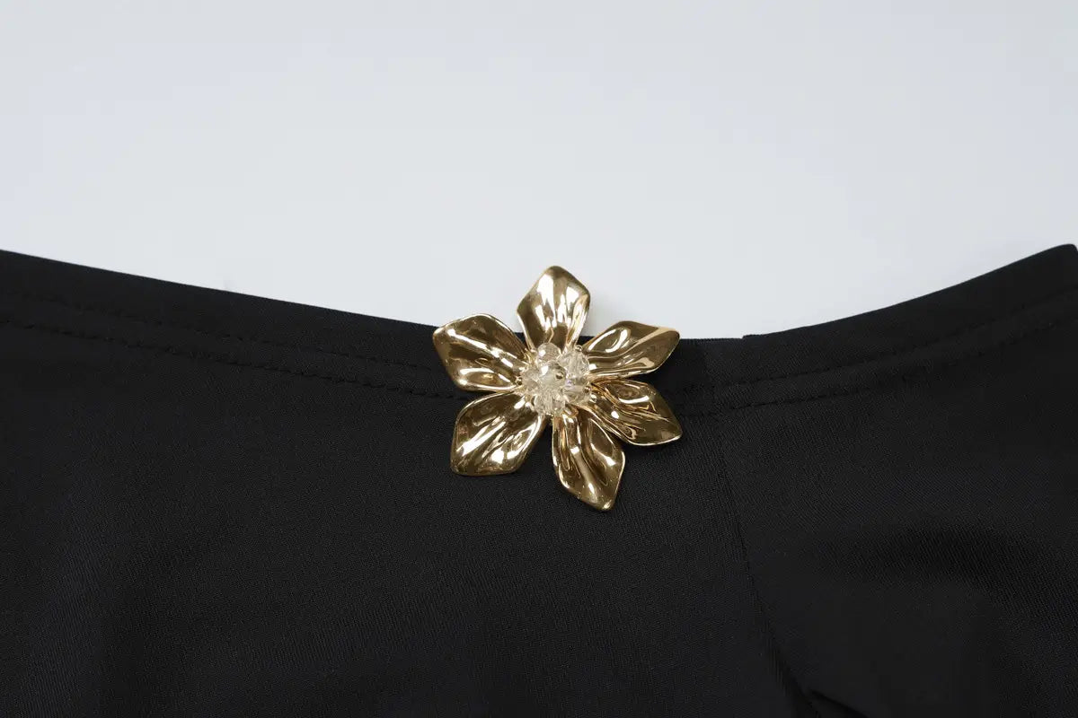 a gold-toned flower-shaped brooch with a clear crystal center adorns the black fabric of a sexy slim oblique shoulder floral mermaid dress