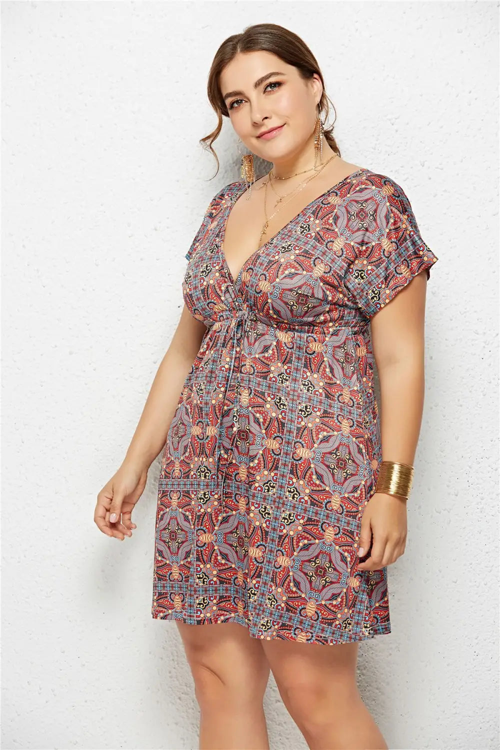 A plus-size woman wears a geometric printed deep v-neck dress with an elastic waist featuring an intricate red blue and beige floral pattern.