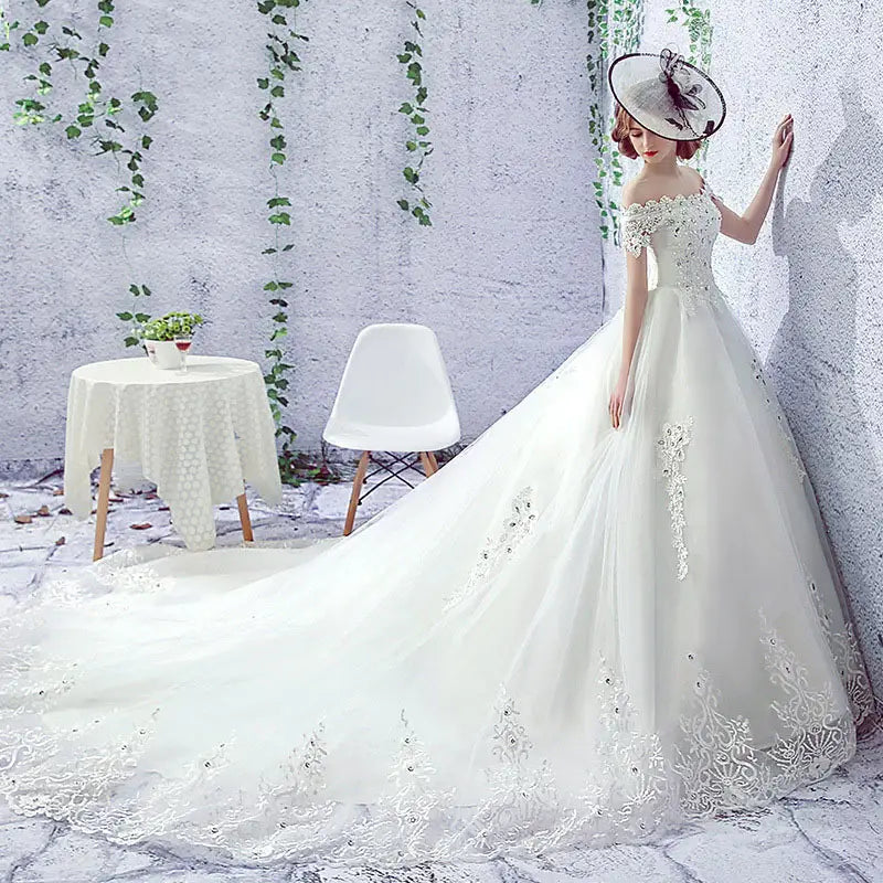 A flowing white lace wedding dress bride featuring off-the-shoulder sleeves and a long train paired with a trailing French veil.