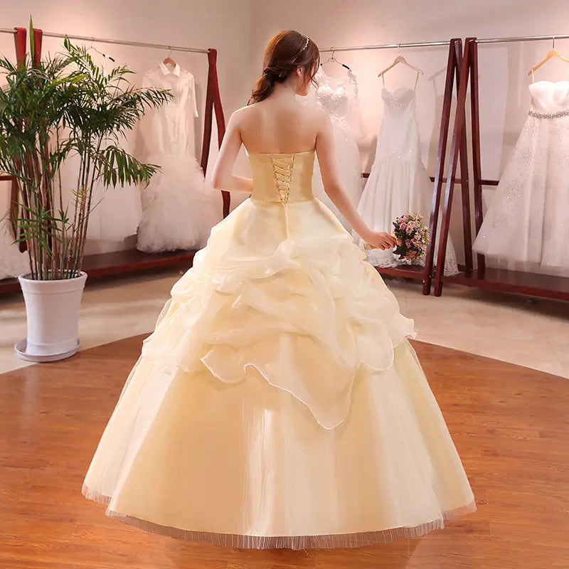 A strapless cream-colored bustier korean princess wedding dress featuring a corseted back and a layered beaded tulle skirt.