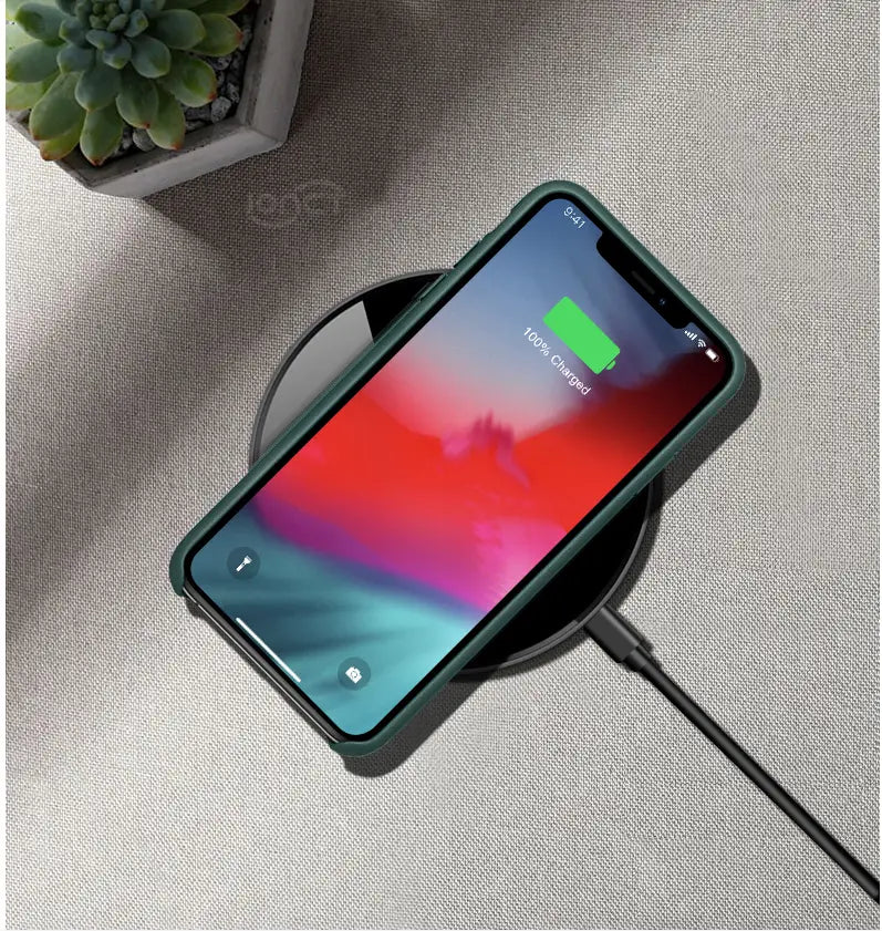 A sleek dark green phone case snugly encasing a smartphone resting on a black glossy 15w smooth wireless charger smooth 15w circular pad.