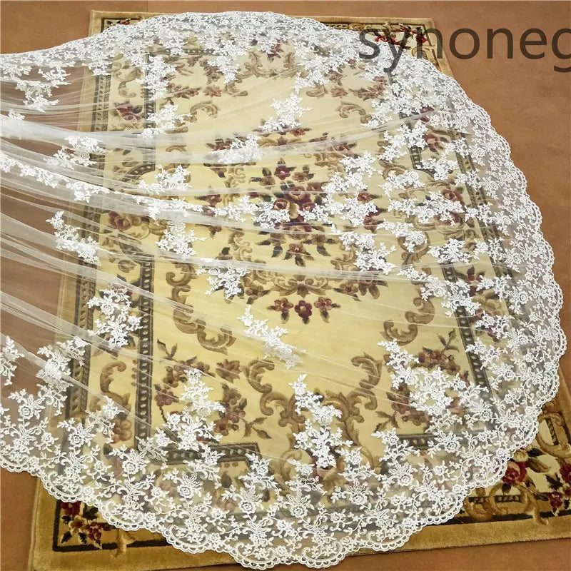 a delicate white lace cathedral length bridal veil with intricate floral embroidery and scalloped edges displayed over a patterned rug