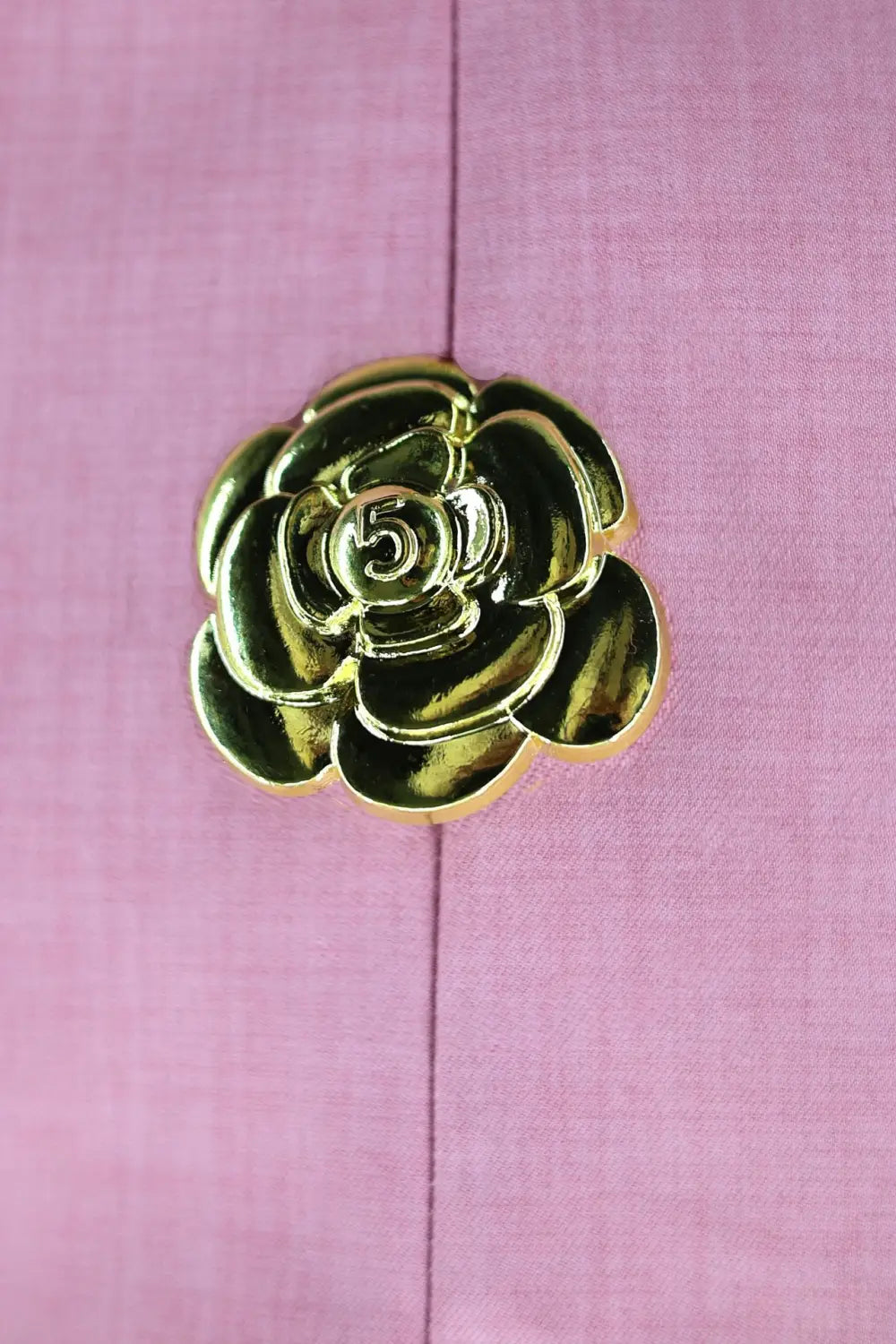 Close up of shiny gold camellia rose button with layered petals on white sleeveless backless dress