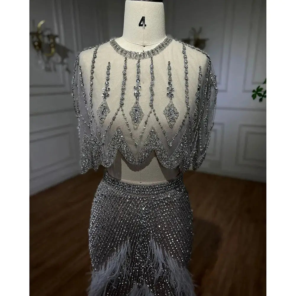 A shimmering silver nude evening dress featuring a two-piece design with a sheer embellished top and a feathered skirt perfect for formal events.