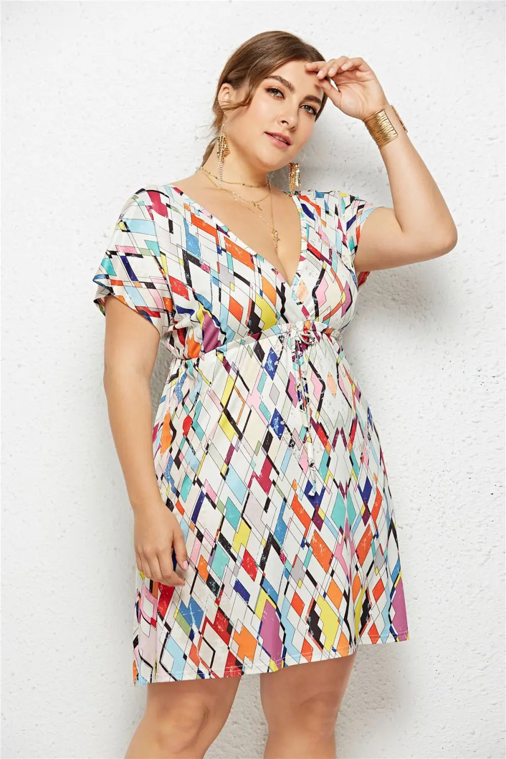 A vibrant plus-size printed deep v-neck dress with an elastic waist featuring a colorful geometric pattern of intersecting diamonds in orange pink blue and yellow on white fabric.