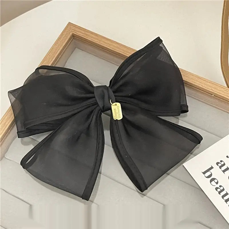 A large elegant black handmade mesh bow hair clip with a gold-colored tag attached to the center knot.