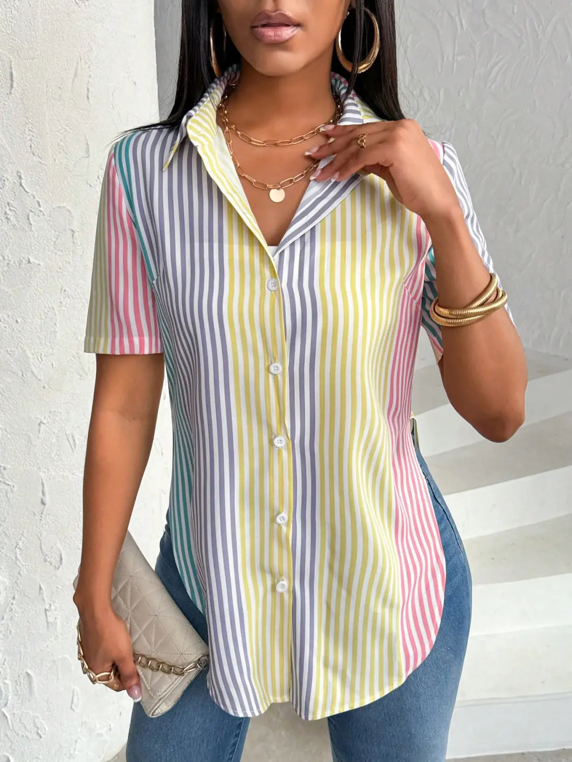 pastel striped short-sleeve button-up shirt with a collared neckline features a contrast color striped asymmetrical hem and multicolored vertical color striped print in shades of yellow, blue, pink, and green.