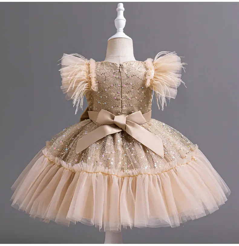 A shimmering gold sequined toddler wedding dress tulle with feathered puff sleeves a layered tulle skirt summer and a beige satin bow at the waist.