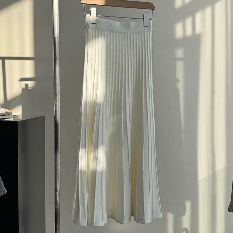 A flowing white pleated midi skirt made of soft lightweight fabric with korean elastic waist and knitted pleated design hanging elegantly on a wooden hanger.