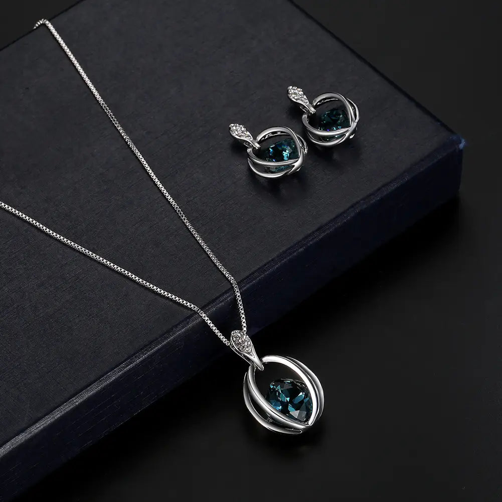 Silver necklace with heart-shaped deep blue crystal pendant and diamond accents paired with matching earrings designed as an elegant crystal bridal necklace featuring fashion inlaid crystal details.