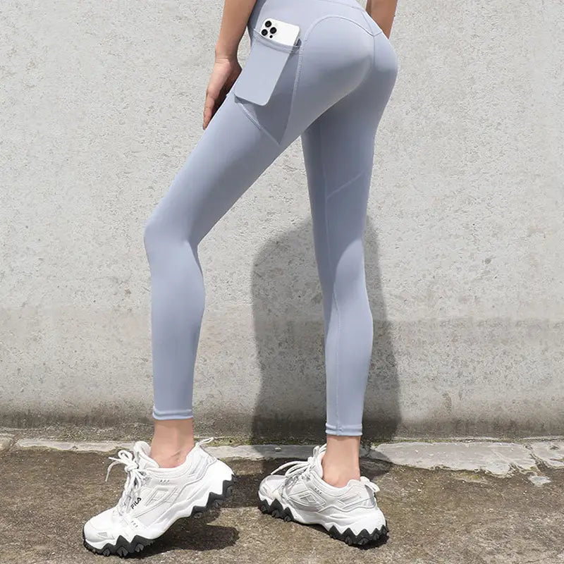 slate blue gym sport seamless leggings in light gray featuring a form-fitting design and side pocket holding a white smartphone.
