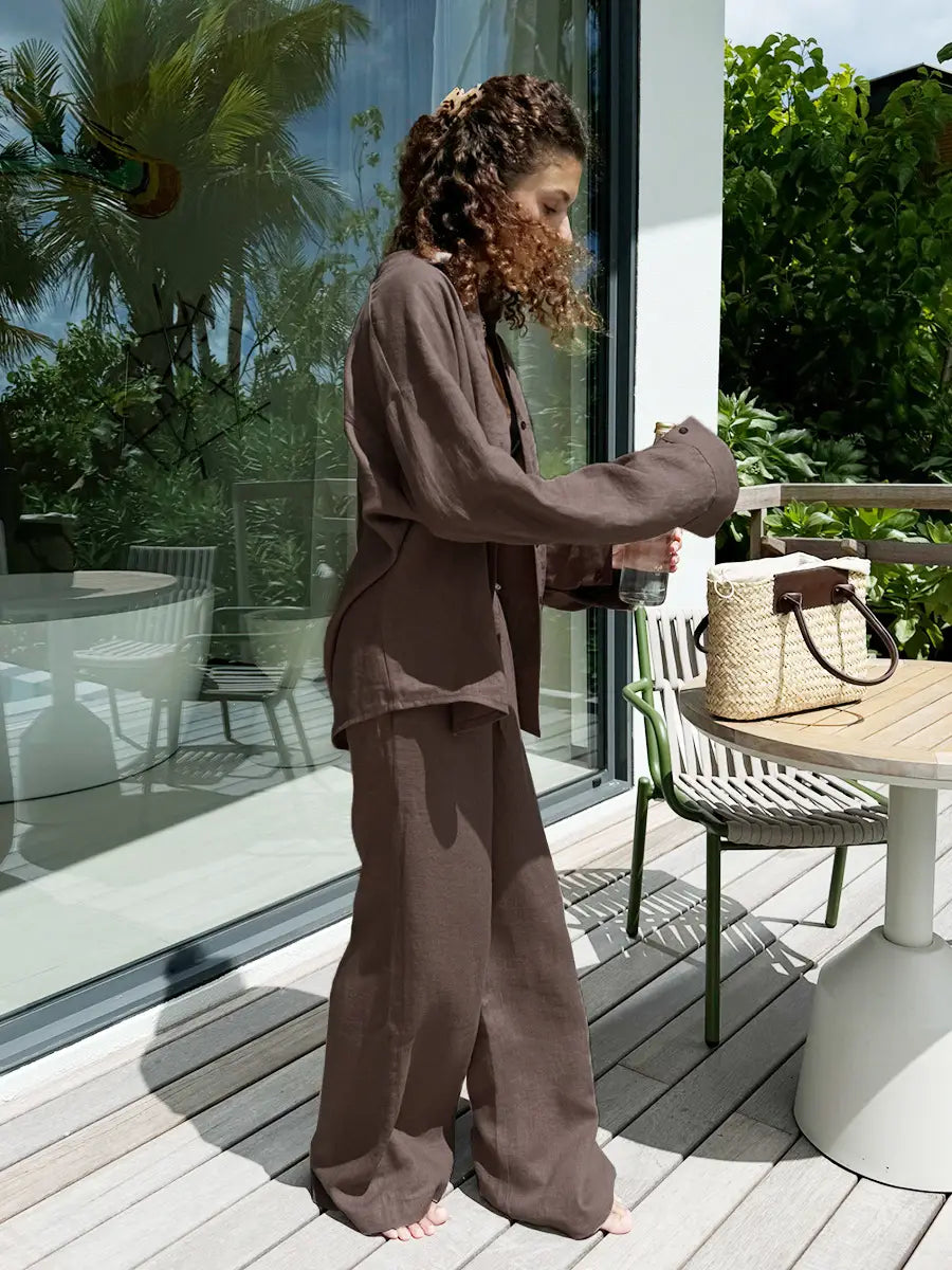 woven straw tote bag with dark brown leather handles and matching top closure paired with white linen long sleeve cotton shirt trousers suit
