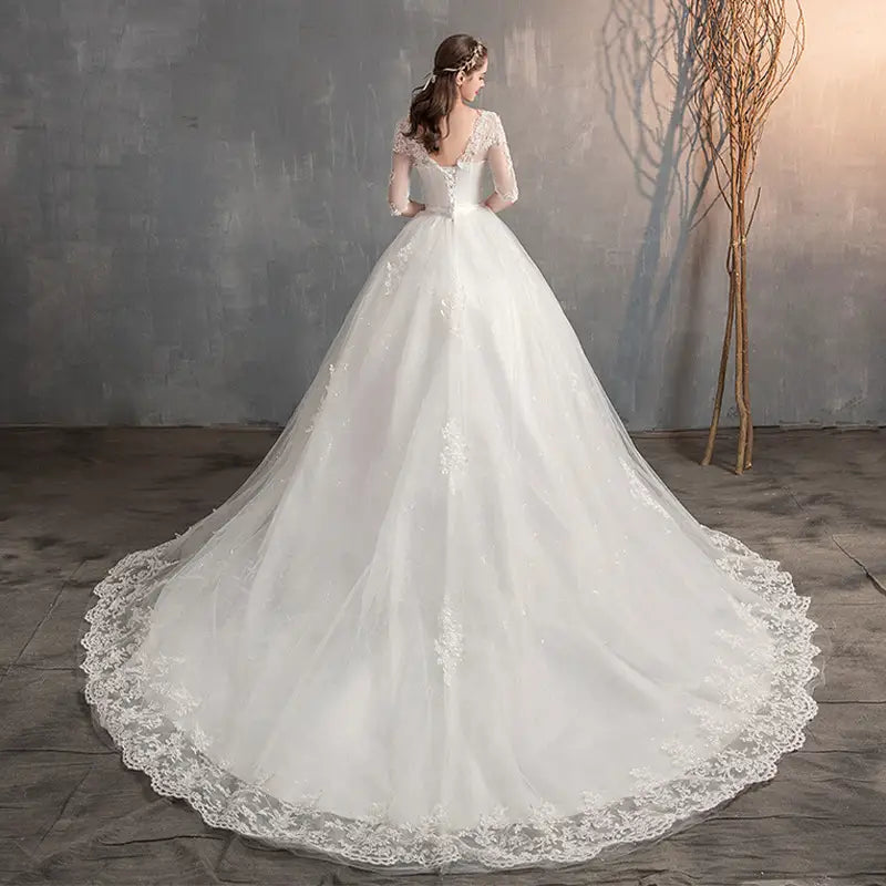 A flowing white high waist wedding dress with delicate lace detailing and a voluminous trailing skirt.