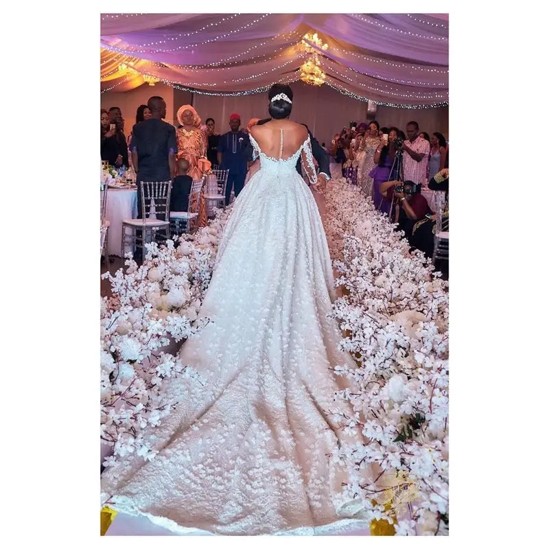 a flowing white lace custom wedding gown with an off-the-shoulder design and a long train adorned with floral embroidery, ideal as a wedding gown bridal dress