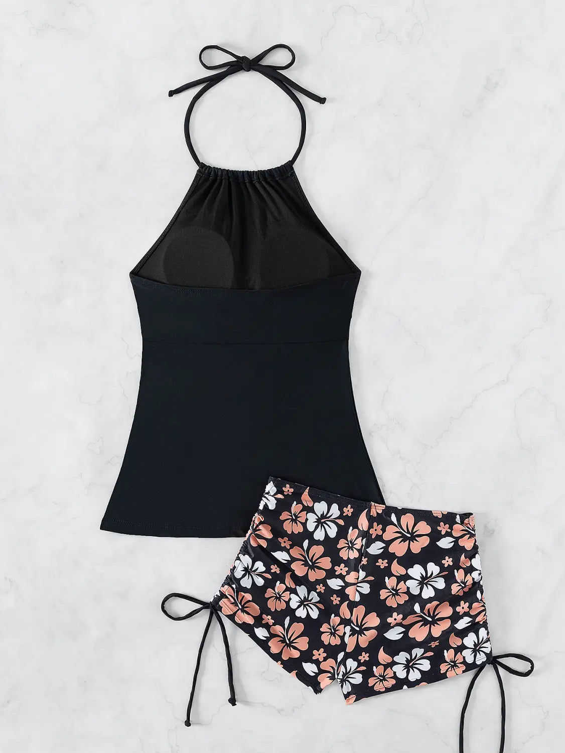 black halterneck printed halter split swimsuit featuring a sheer mesh panel halter top and matching floral print shorts with peach and white hibiscus flowers on a dark background