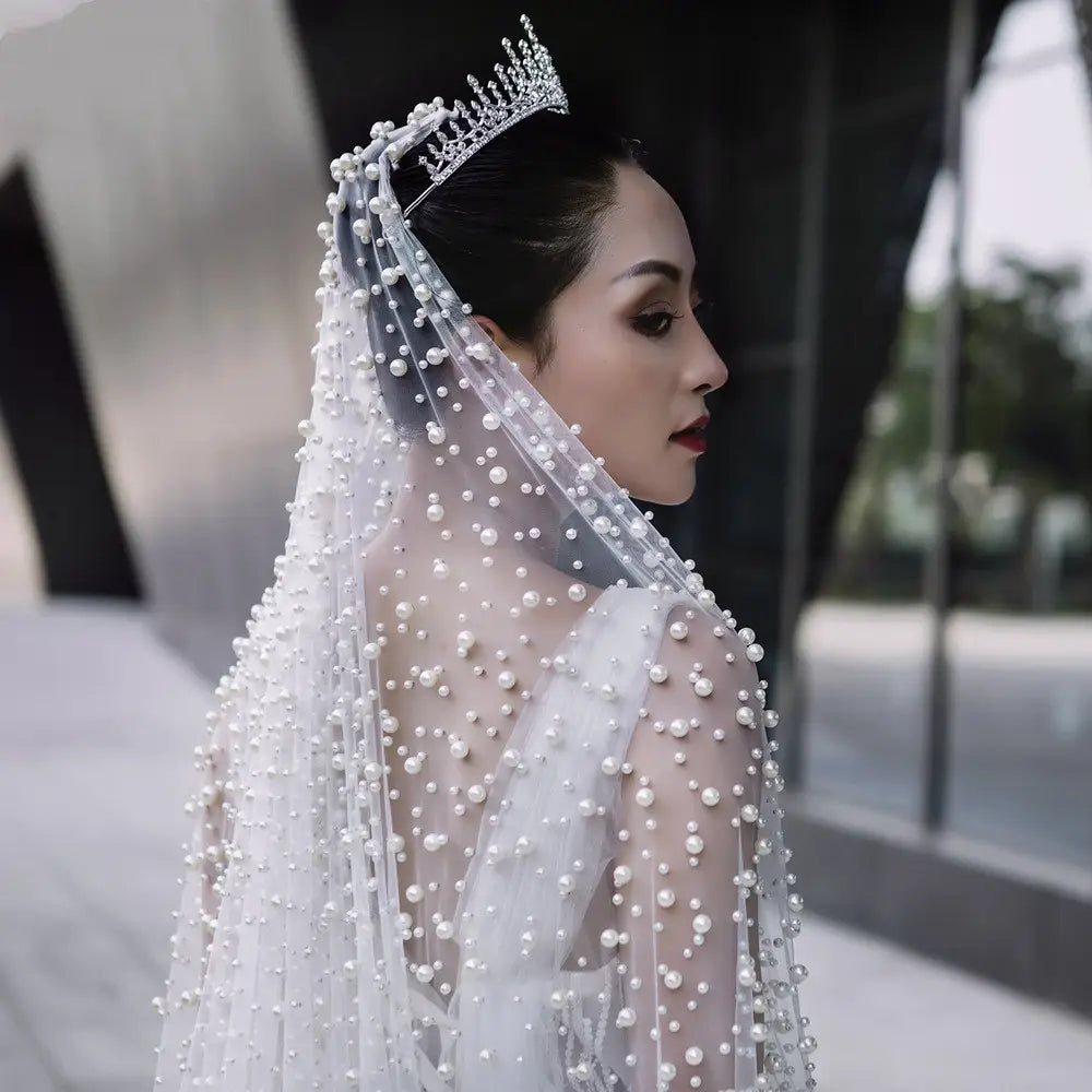A sparkling silver luxury heavy industry bridal tiara adorned with intricate diamond-like embellishments and a cascade of white industry bridal pearl veil.