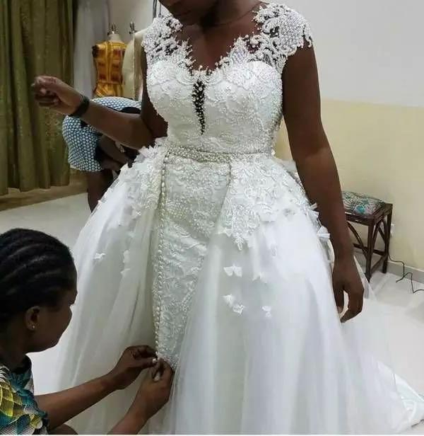 A white lace african mermaid detachable wedding dress with intricate beading and a fitted bodice.