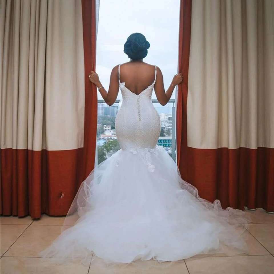 A white lace sleeveless big tail african mermaid wedding dress featuring a fitted bodice with delicate spaghetti straps and an intricate lace back detail showing the back side of the gown made from main fabric.
