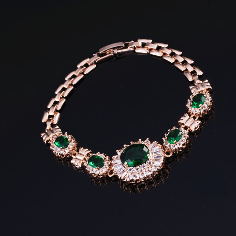 A rose gold bracelet from the big brand retro zircon four-piece suit features a central oval emerald surrounded by sparkling clear stones, flanked by smaller green gemstones and intricate metalwork.