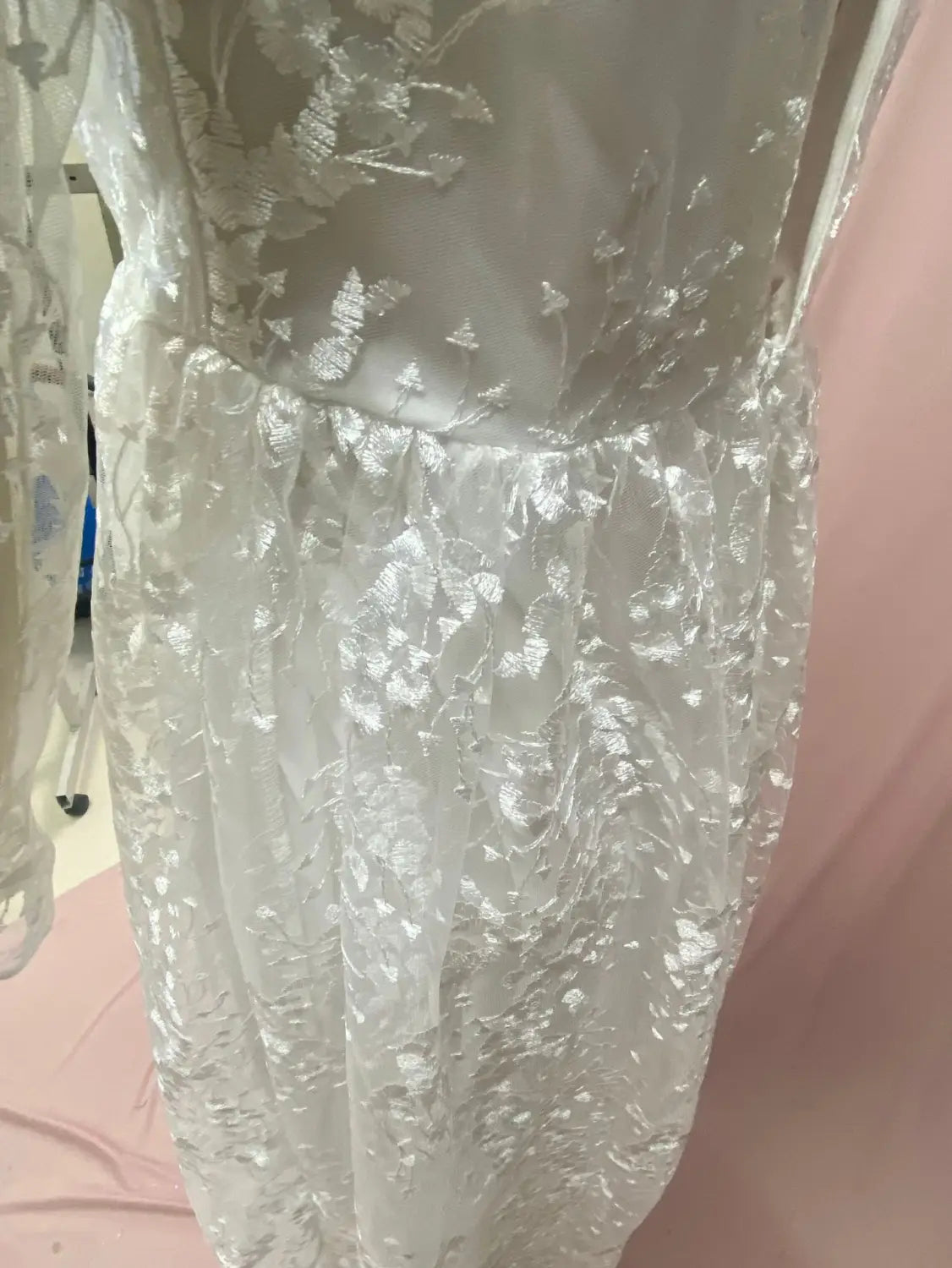 A delicate white long sleeve wedding dress lace gown with intricate floral embroidery and a sheer flowing skirt.