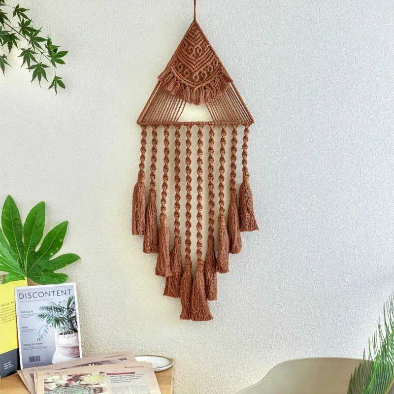 A terracotta-colored handwoven home decor triangle dream featuring intricate macrame patterns and dangling tassels for decorative wall display.