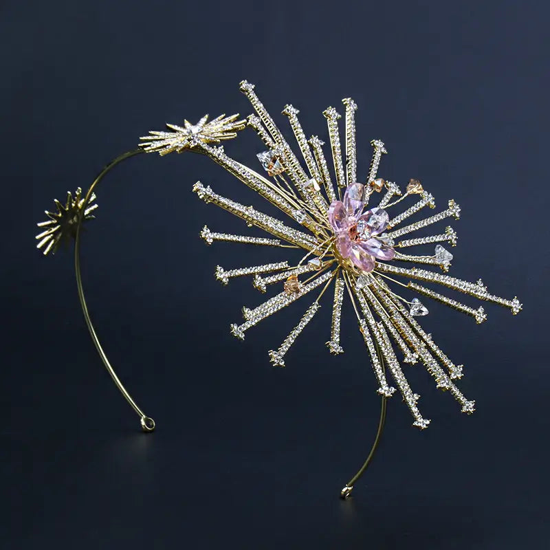 A delicate gold-toned bridal rhinestone headband featuring a radiant starburst design with clear crystals and a central pink gemstone flower hair accessory.