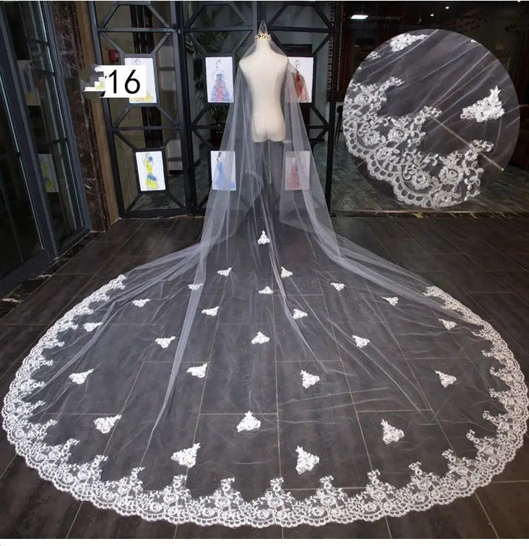 A long flowing white lace bridal wedding dress veil with intricate floral embroidery and scalloped edge in wide style featuring a hair comb.