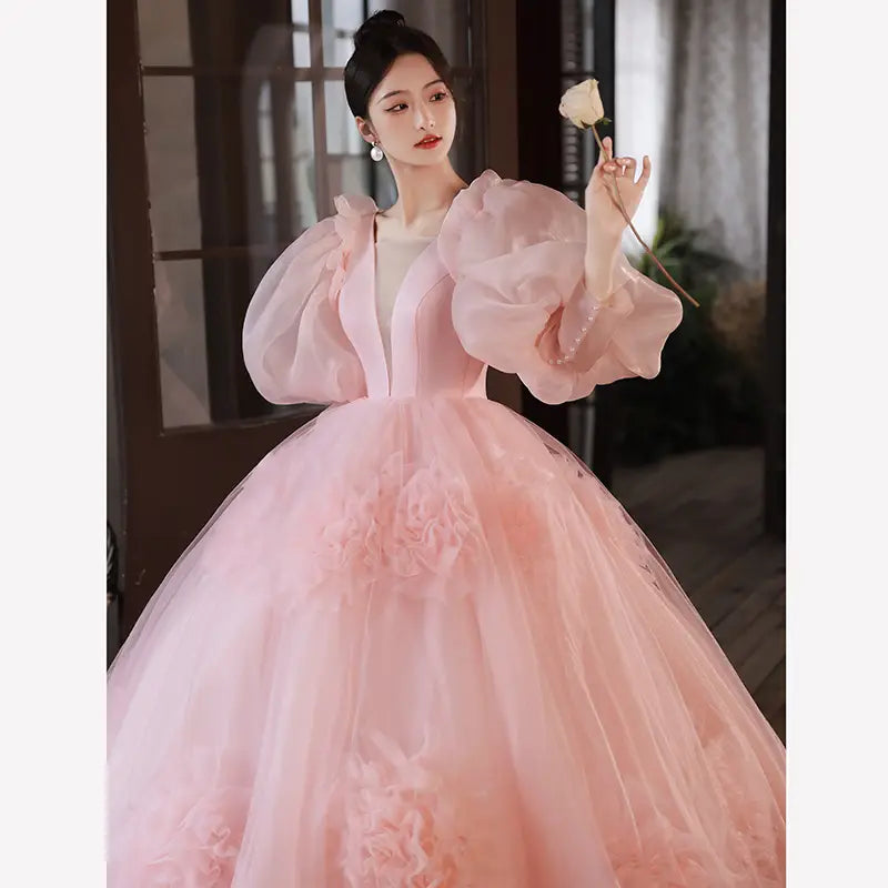 A delicate blush pink high end banquet style host gown featuring voluminous puffy sleeves and a flowing floral appliqué tulle skirt.